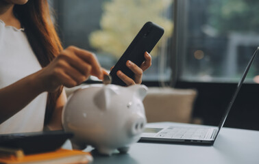 Young Asian woman saving for retirement Saving money through a piggy bank and taking notes on...
