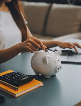 Young Asian woman saving for retirement Saving money through a piggy bank and taking notes on notebook, savings concept.