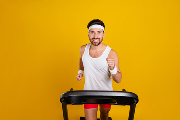 Photo of funky excited guy sportswear running treadmill empty space isolated yellow color background