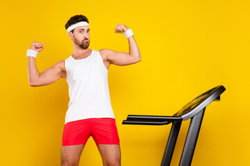 Portrait of confident powerful person treadmill equipment flexing biceps isolated on yellow color...