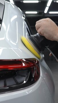 A mechanic polishes the surface of a white car body. Vertical video. 