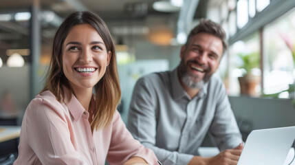 Two colleagues share a light-hearted moment, smiling and engaging in a discussion during a collaborative office meeting, suggesting a positive and productive work environment.