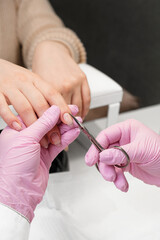 Close up shot of a nail technician cutting the cuticle with scissors. Beautitian in pink gloves and white coat in a process of nail preparation.