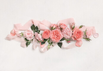 Romantic falt lay with light pink roses, petals and buds, green leaves and silk ribbons top view on white