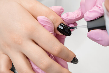 Applying top coat with golden glitter on a black nail polish, close-up. Painting nail polish by...