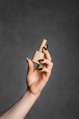 Woman's hand holding beige nail polish bottle against gray background.