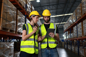 Two distribution warehouse coworkers are walking using a digital tablet to check inventory on a...