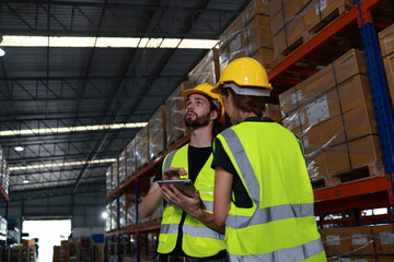 Two distribution warehouse coworkers are walking using a digital tablet to check inventory on a...