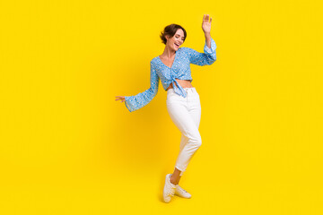 Fototapeta na wymiar Full size photo of good mood adorable girl wear stylish blouse white pants dancing at summer party isolated on yellow color background