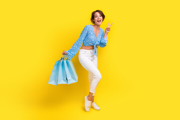Full size photo of positive funky woman wear blue top hold shopping bags show v-sign symbol say hi...