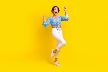 Fototapeta na wymiar Full size photo of satisfied ecstatic girl wear stylish blouse white pants win bet clenching fists isolated on yellow color background