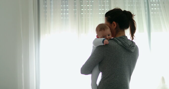 Real life mother holding newborn baby at home next to curtain window