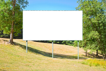 Blank advertising signboard in a green field with trees on background - concept with copy space for text inserting