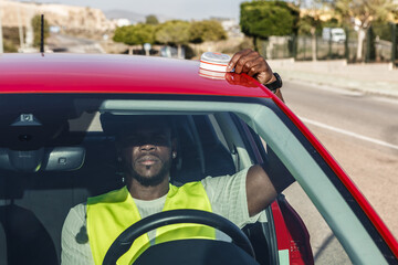 Fototapeta na wymiar Man in Yellow Vest Driving Red Car Signals Car Breakdown With V16 Emergency Light