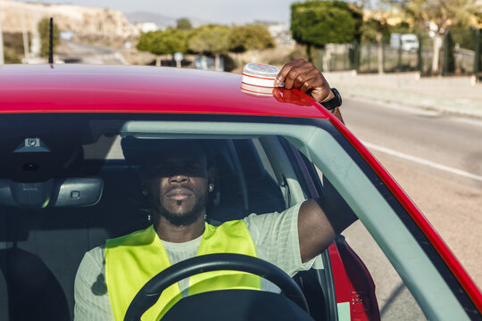Man in Yellow Vest Driving Red Car Signals Car Breakdown With V16 Emergency Light