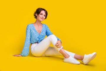 Full size photo of adorable gorgeous optimistic woman wear blue top white trousers sit on floor isolated on yellow color background