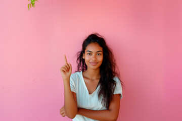 Young brunette with long hair and a white shirt pointing up with her hand on a pink background