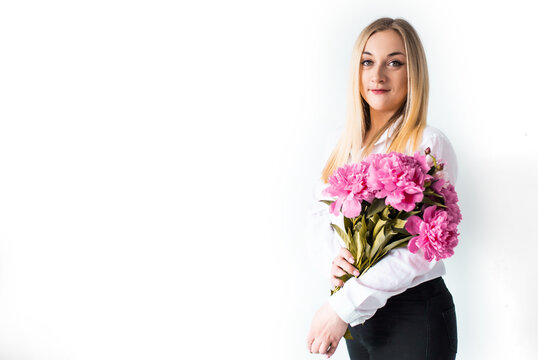 Woman holds peony flowers agains white wall. Young girl with spring summer bouquet bouquet. Lifestyle photo with flowers and a copy space.