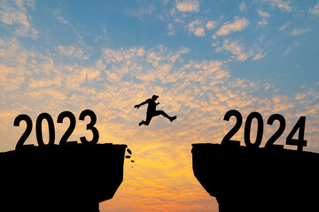 Man jumping on cliff 2024 over the precipice with stones at amazing sunset. New Year's concept....