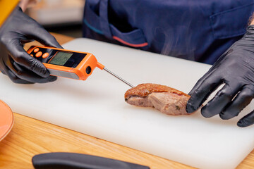measuring the temperature of a beautiful piece of roasted duck breast steaming on white board