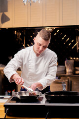 a chef in a professional kitchen using tongs turns a beef steak over hot frying pan with oil