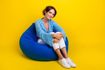 Full size photo of cheerful gorgeous woman wear blue top sitting on bean bag embrace her knees...