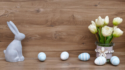 Fröhliche Osterkulisse mit Ostereiern, Blumen und Osterhasen vor einer Holzwand mit Platz für...
