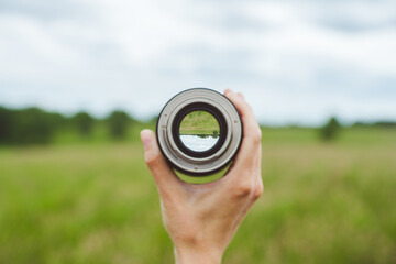 Looking to the green summer field through lens in hand. Point of view. Selective focus.