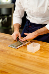 close-up of a chef in a white jacket in the kitchen at the table sharpens a knife on a green stove