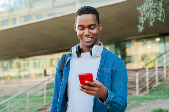 Portrait of a african american male student having fun with a cellphone posting on the social media. Real teenage guy smiling using a smartphone. Young man with a mobile phone. Teen schoolboy. High