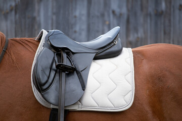 black leather saddle on the back of a horse against the background of a wooden stable. equestrian...