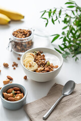Granola or muesli with yogurt and banana on a white wooden table with branch.
