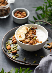 Healthy breakfast. Homemade granola or muesli with banana and nuts in a bowl on a dark  background with branch.