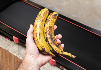 Bananas in a man’s hand against the background of a treadmill in a gym, weight loss concept