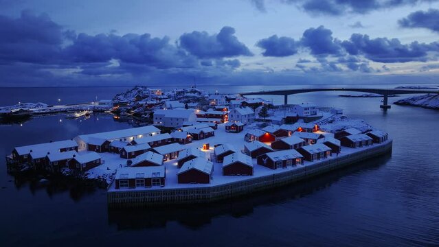Drone Footage Reveals Snow-Covered Mountains, Rorbuer, and Fjords in Winter Night at Lofoten Islands, Norway.
