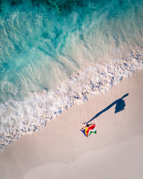 Aerial picture of a woman holding a Seychelles flag on a tropical beach with turquoise sea and waves 