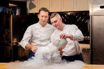 two chefs in white uniforms are preparing liquid nitrogen in the kitchen which spreads all over table