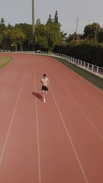 Camera tracking of a runner in an Olympic competition stadium. Vertical drone video with copy space for text. Sport and health concept