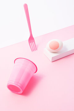 Pink painted easter egg with plastic fork and cup on pink background