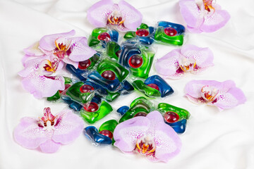 Laundry capsules among orchid flowers on satin fabric.