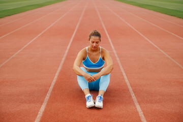 Fototapeta premium Woman sitting and relaxing on the running track at the sports arena