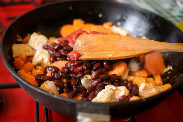 Making dinner at home. Cooking tasty stewed vegetables and beans with white chicken meat on the frying pan
