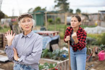 Obraz premium Two upset young and old female neighbors disagree with each other while digging garden on smallholding in autumn