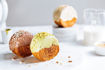 Fusion croissant called Cromboloni invented in New York. Round puff pastry filled with cream, and glazed with white, milk chocolate or pistachio. Crunchy and soft in the same time. Bright background. 