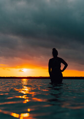 silueta de chica en bikini con mano en la cintura en amanecer dentro de laguna de bacalar viendo el amanecer, quintana roo con cielo y nubes con textura