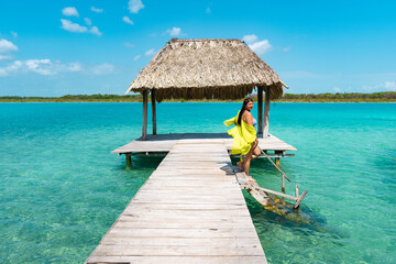 Chica joven en muelle en traje de baño amarillo de vacaciones bajando escalones a la laguna de bacalar