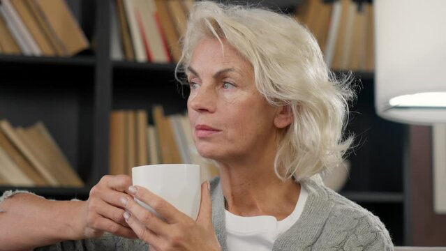 Portrait senior woman drinking tea. Good looking gray haired old lady with cup coffee in hands enjoy favorite beverage looking at something sitting at home. Leisure, pastime resting relaxing concept.