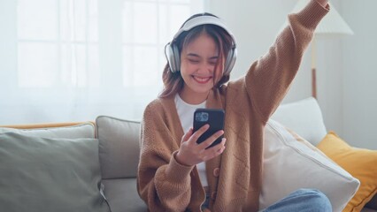 Happy asian woman listening to music from mobile phone while sitting on the the sofa at homes, Smiling girl relaxing with headphones in morning, Time to relax. - Powered by Adobe