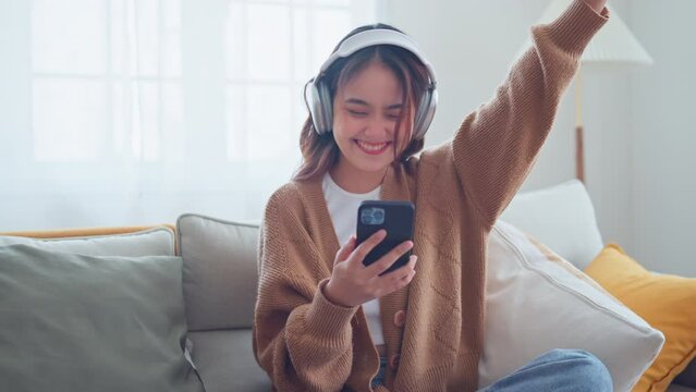 Happy asian woman listening to music from mobile phone while sitting on the the sofa at homes, Smiling girl relaxing with headphones in morning, Time to relax.