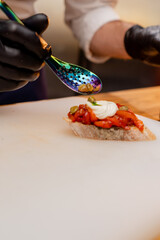 close-up of chef's hands in black gloves spooning capers on a pepper sandwich